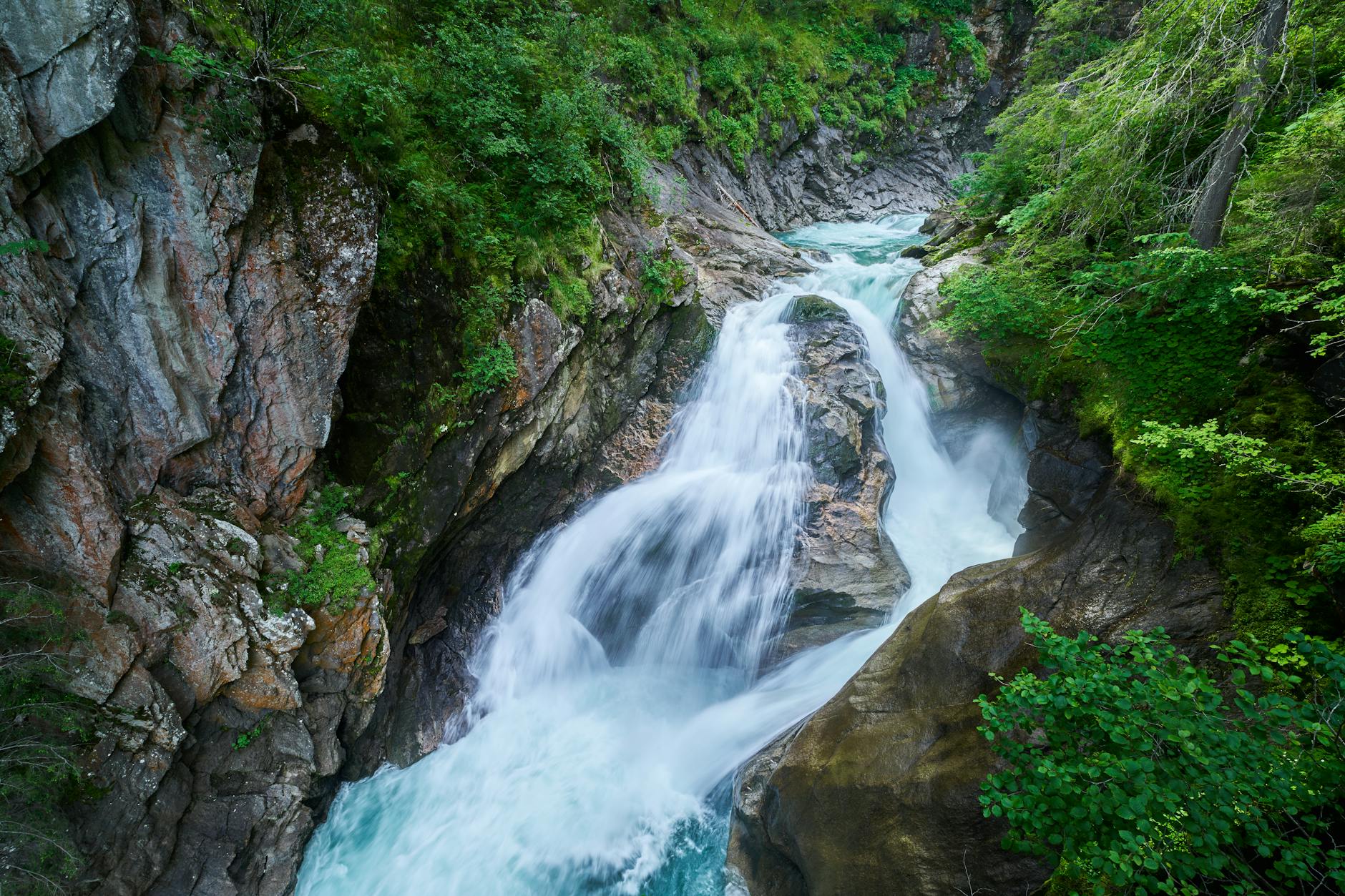 Scenic view of Krimml waterfall cascading through rocky terrain in lush Austrian forest.