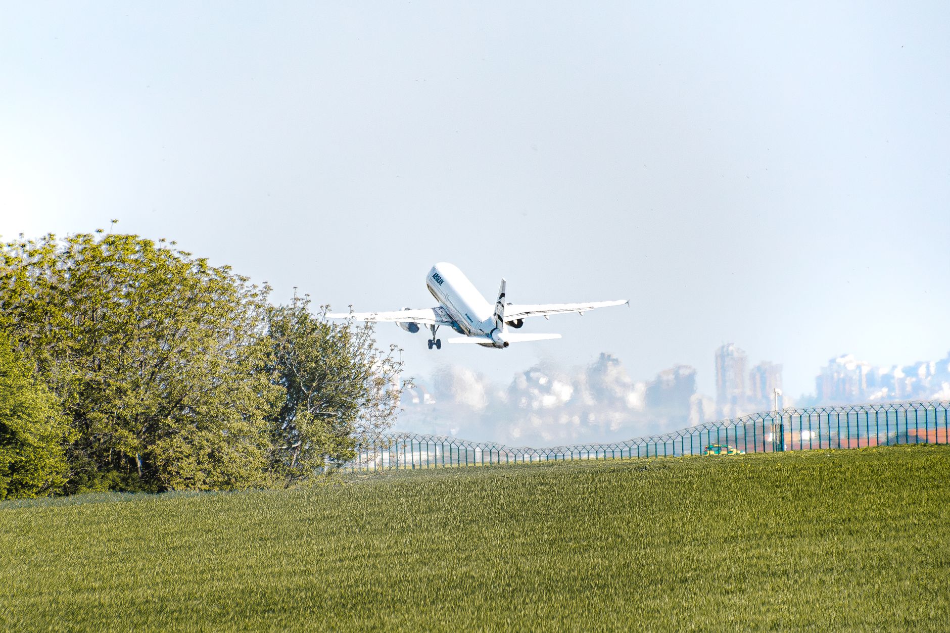 An airplane takes off over lush greenery with Beograd's urban skyline in the background.