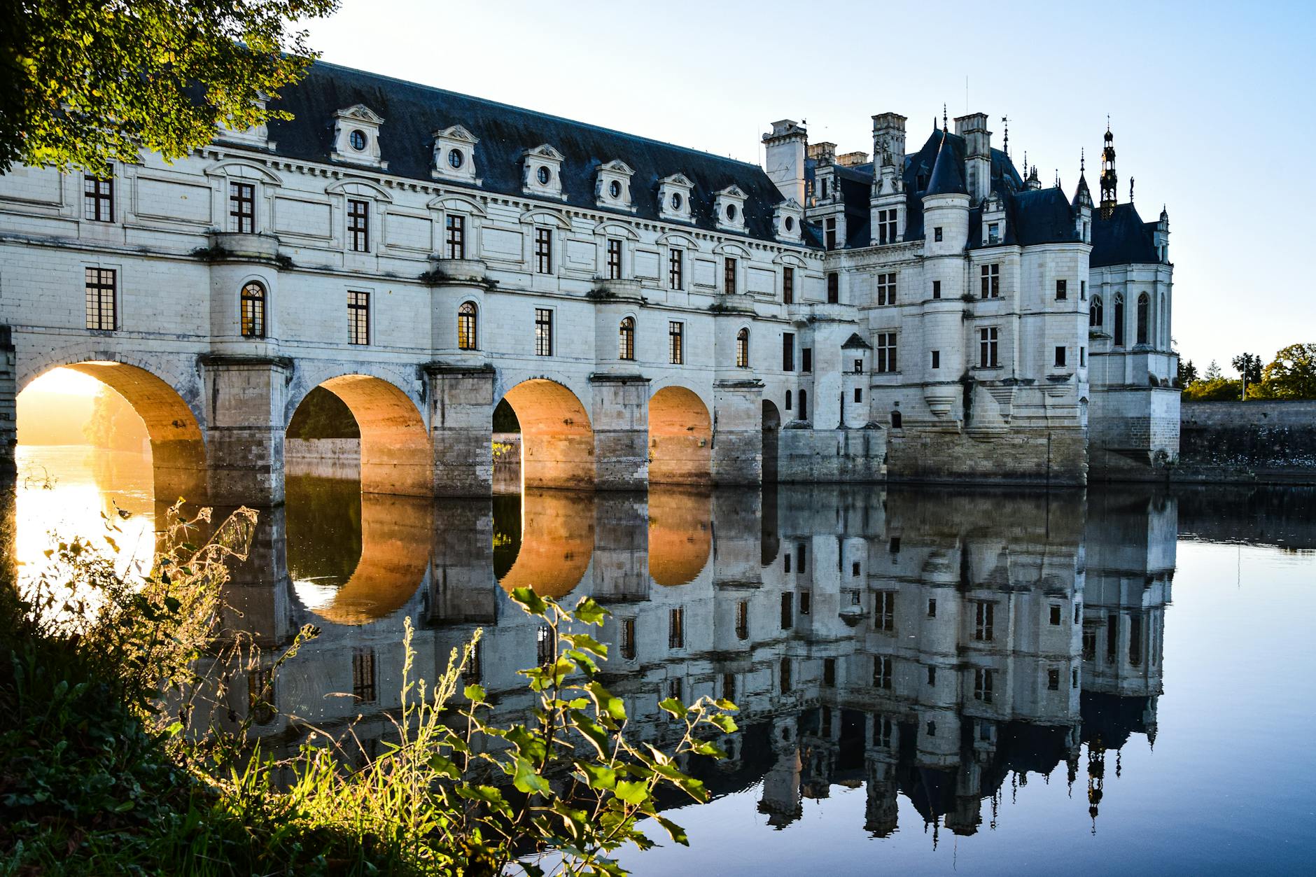 Elegant reflection of Château de Chenonceau on the Cher River at sunrise in the Loire Valley.