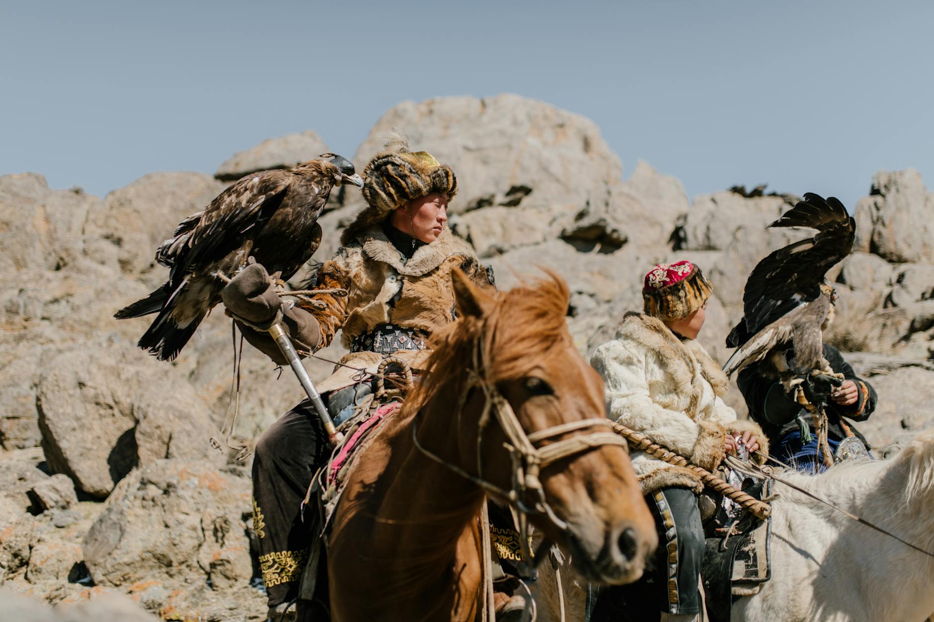 Traditional Mongolian eagle hunters riding horses in rocky terrain.
