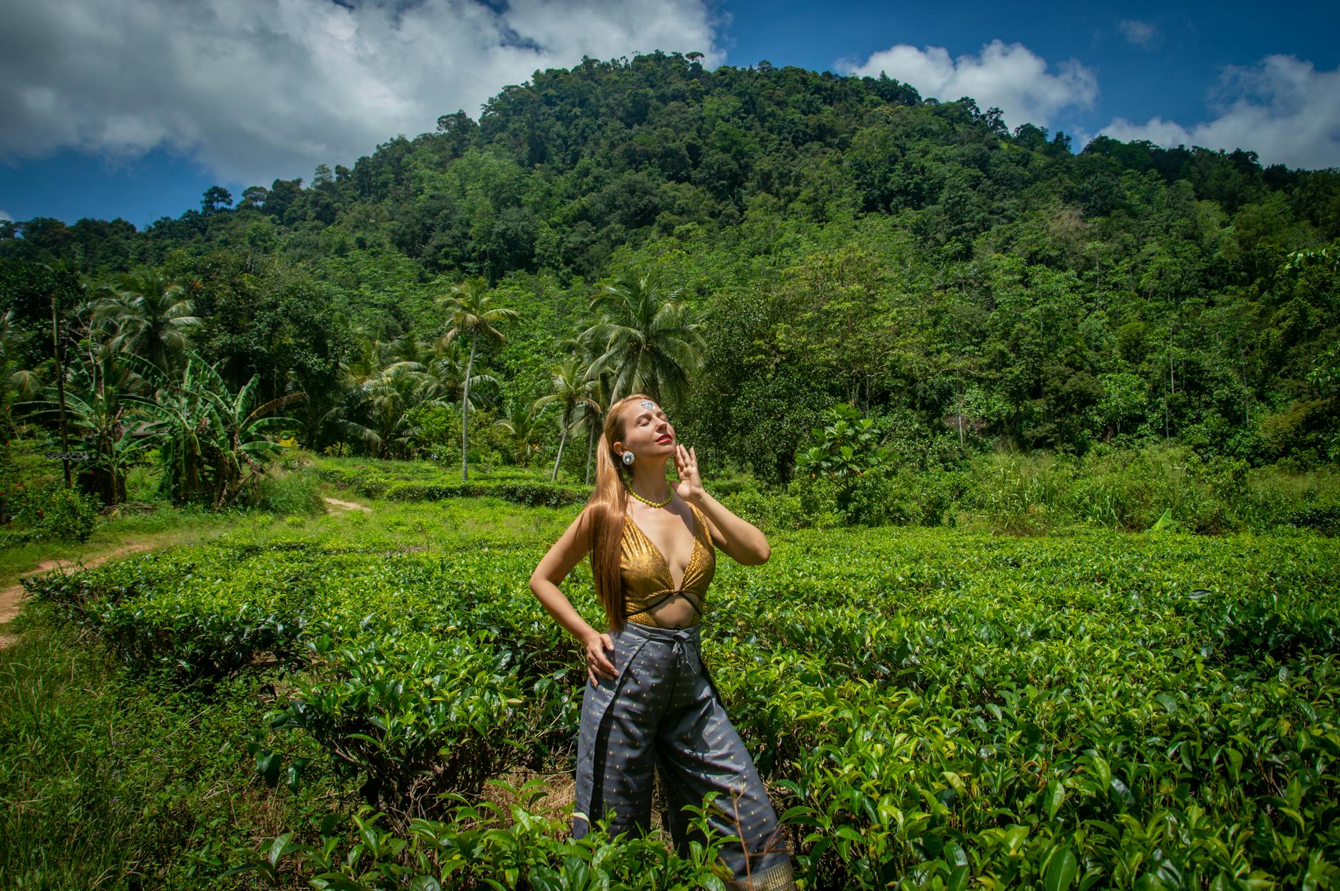 A woman standing in a lush tropical tea plantation, basking in the sunlight beneath vibrant green hills.