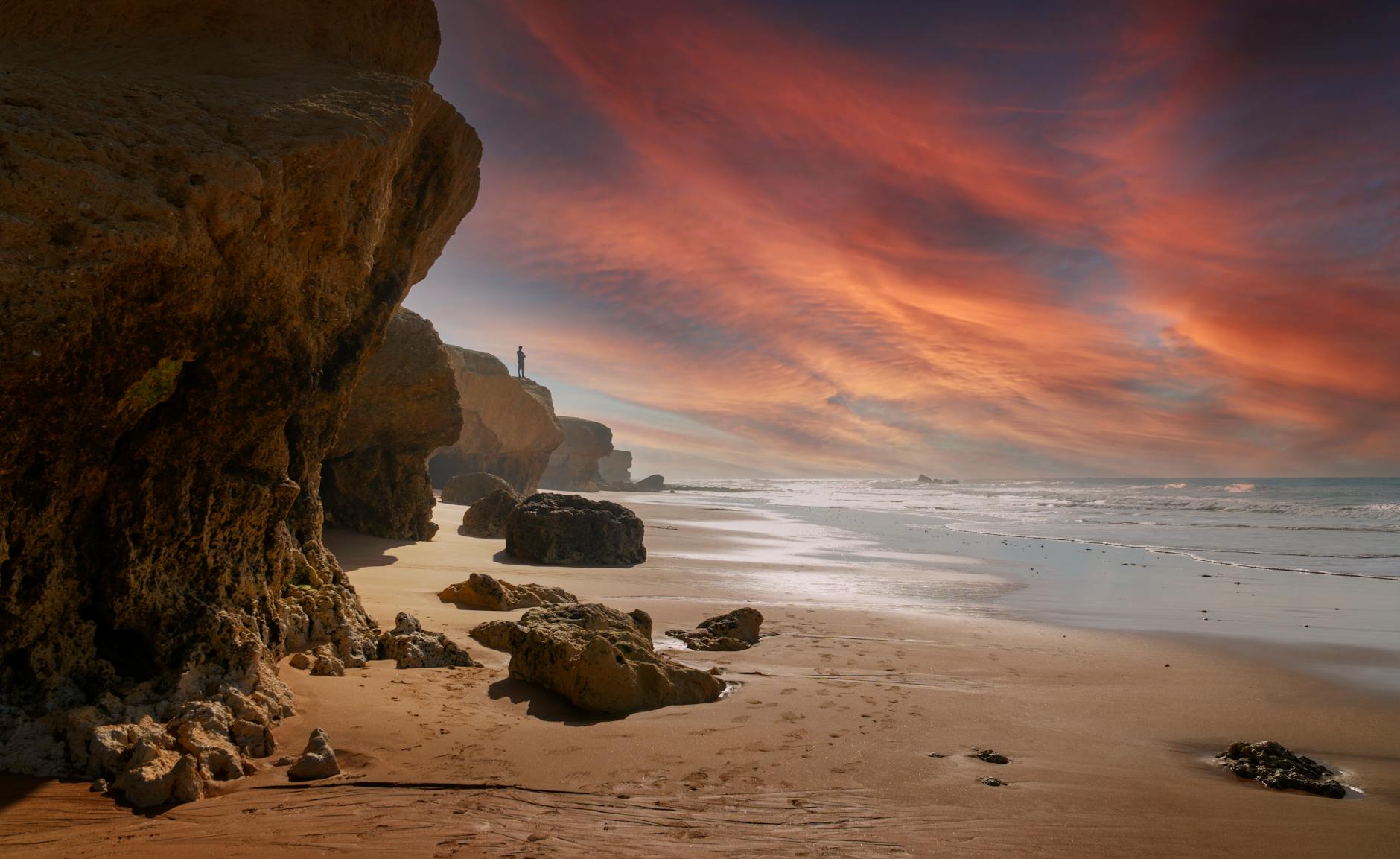 A stunning view of the Faro coastline with dramatic rock formations and a vibrant sunset sky.