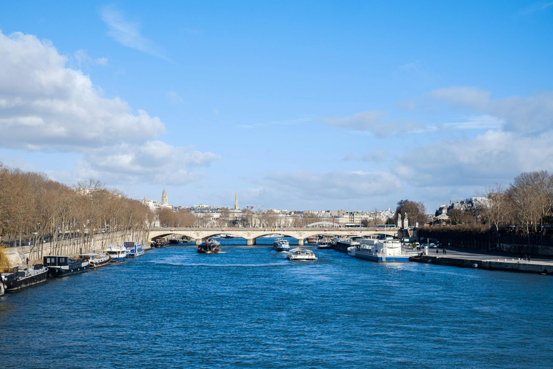 Beautiful view of the Seine River with boats and bridges under a blue sky in Paris, France.